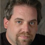 Headshot photo of man with short brown hair with mustache and short beard