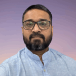 Headshot photo of man with short dark hair, dark full mustache and beard and glasses.