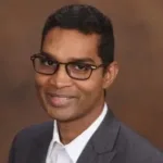 Headshot of smiling man with short black hair and glasses.