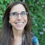 Headshot photo of smiling women with long straight brown hair and wearing glasses